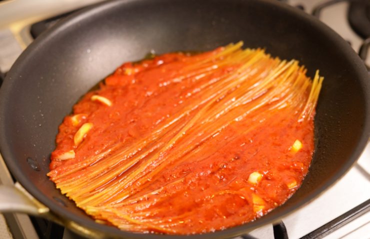 spaghetti che cuociono in padella con pomodoro