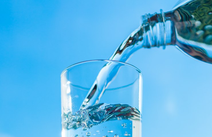Acqua minerale versata da una bottiglia in un bicchiere di vetro