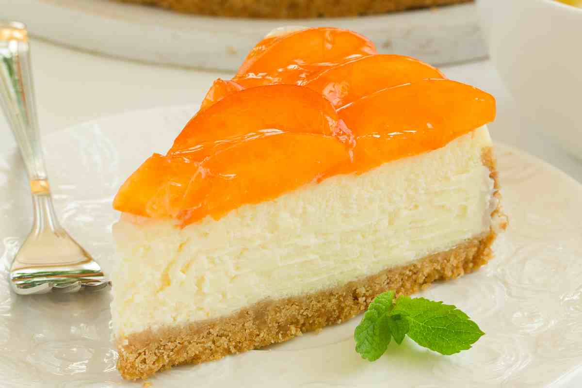 fetta di cheesecake alle pesche in un piatto con una foglia di menta