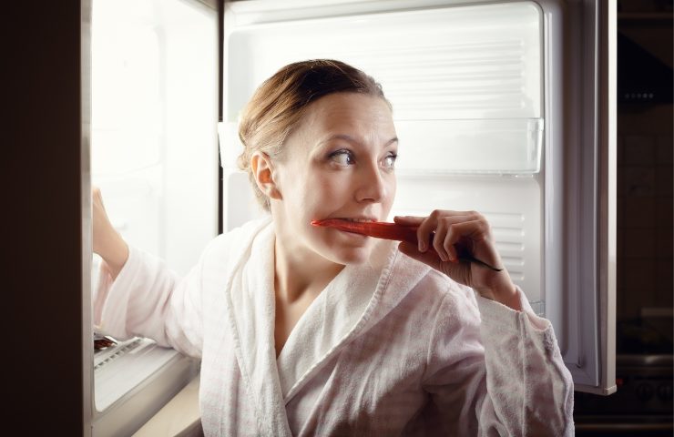 Una donna che mangia davanti al frigo di notte