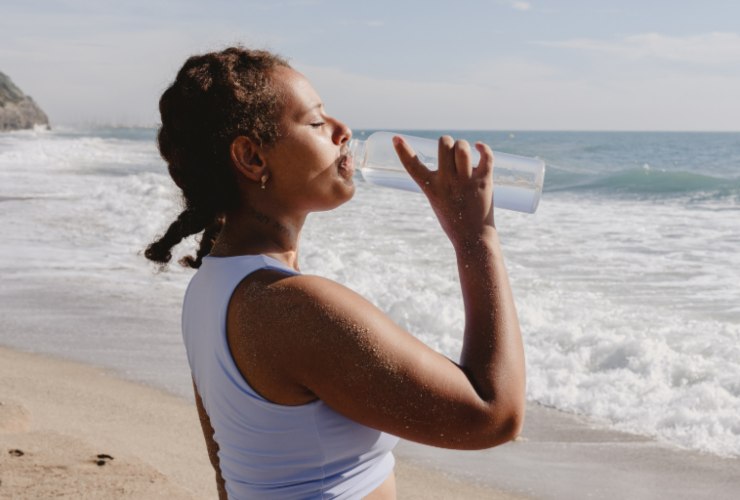 Donna che beve acqua in spiaggia