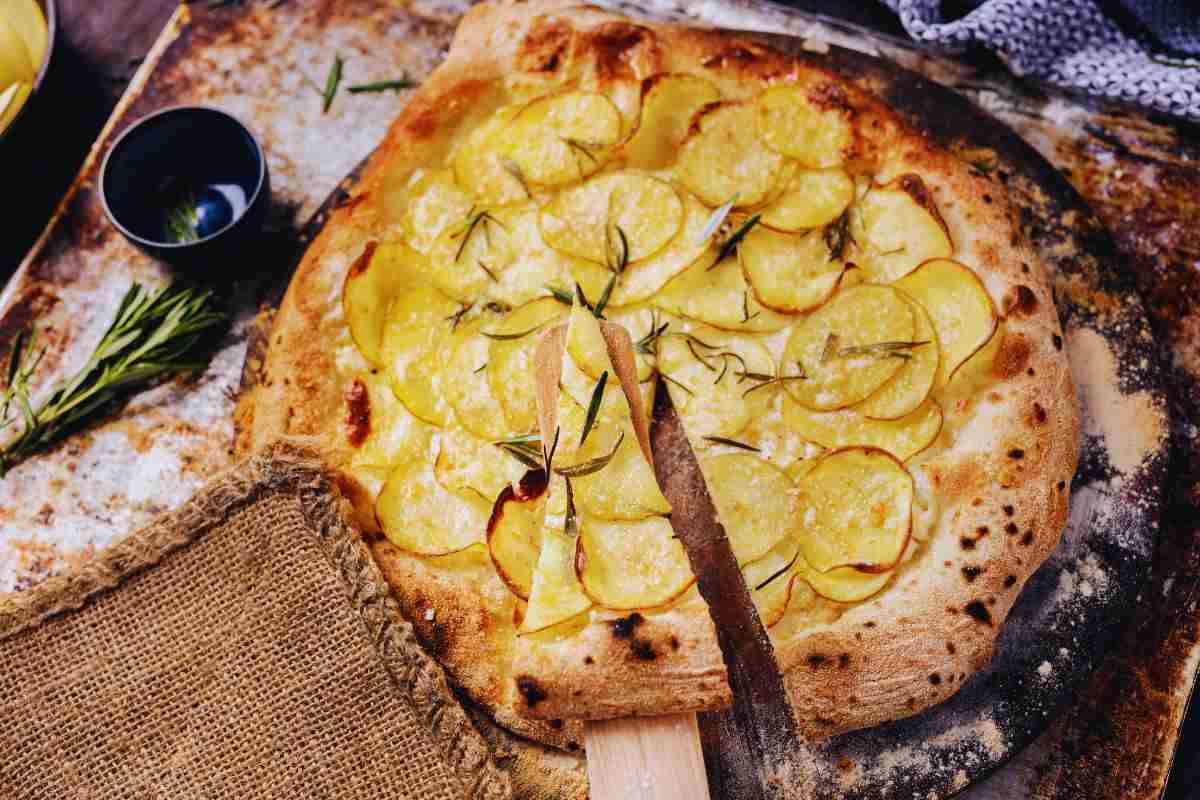 fetta di focaccia tagliata dalla tonda con le patate sul piano di lavoro