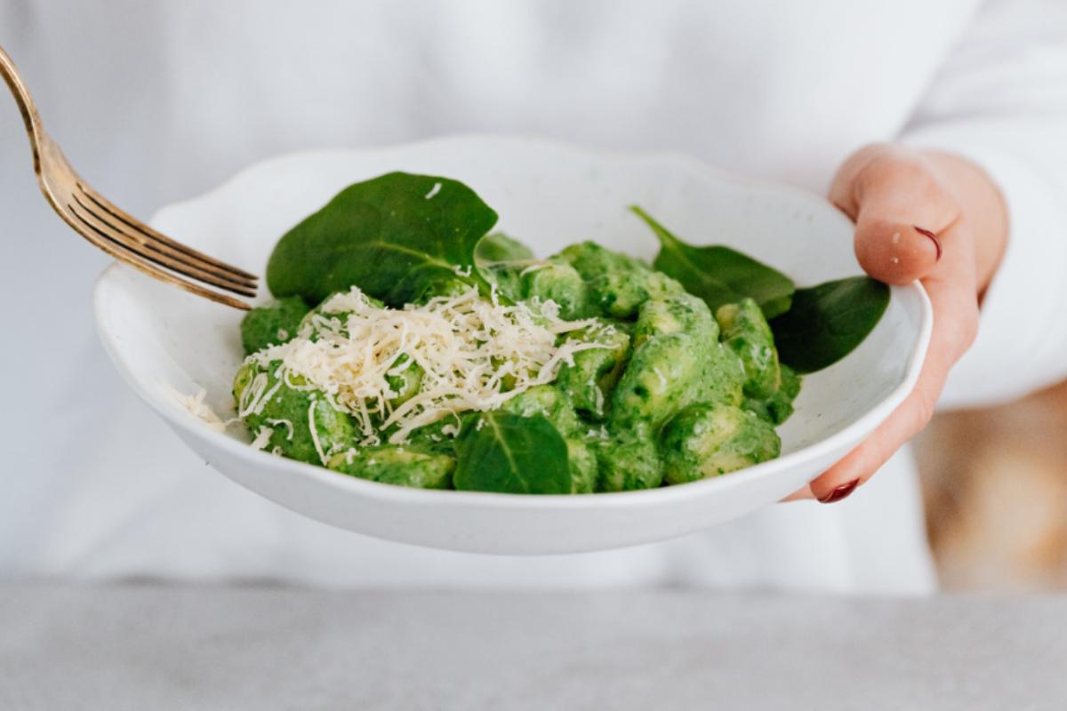 mani reggono piatto con gnocchi agli spinaci cremosi