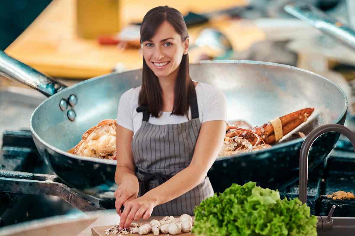 Una donna che cucina ed una padella con cibo sullo sfondo