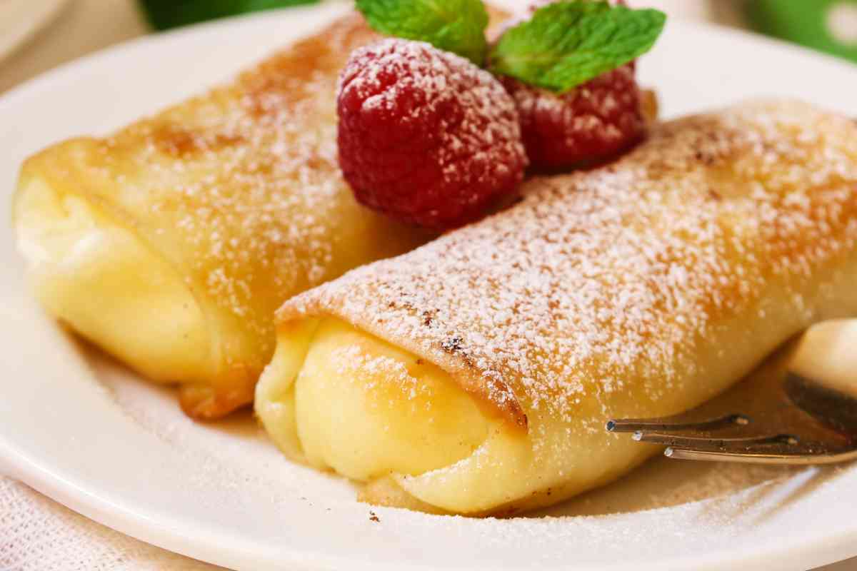 due crepes farcite con la crema pasticcera e decorate con lamponi e zucchero a velo in un piatto