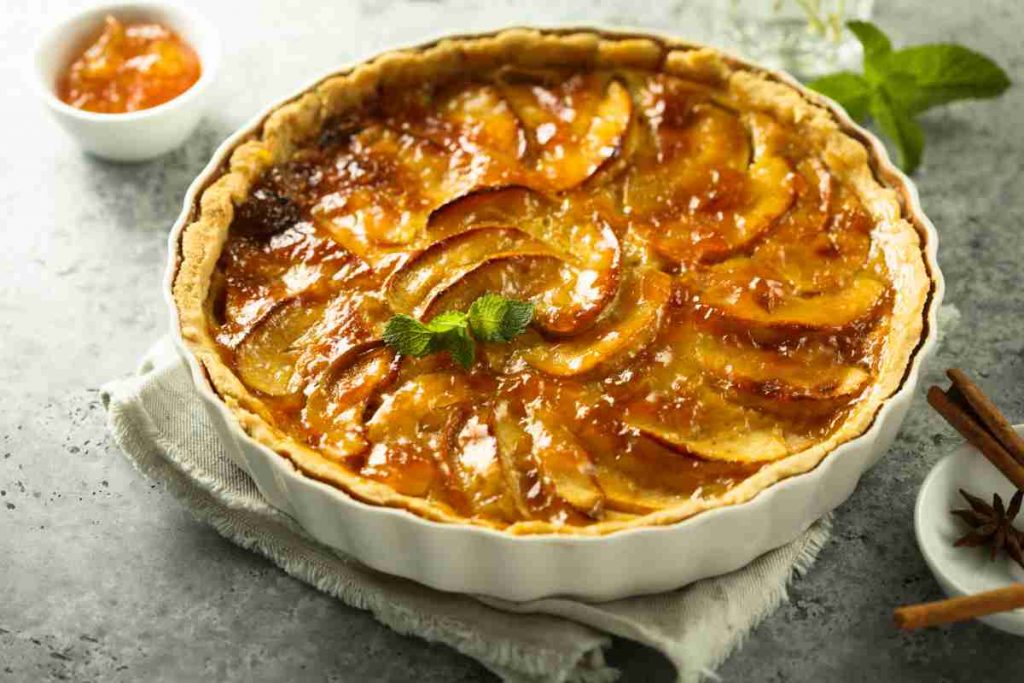 pirofila tonda con dentro la crostata di mele e marmellata con vicino una ciotolina di marmellata
