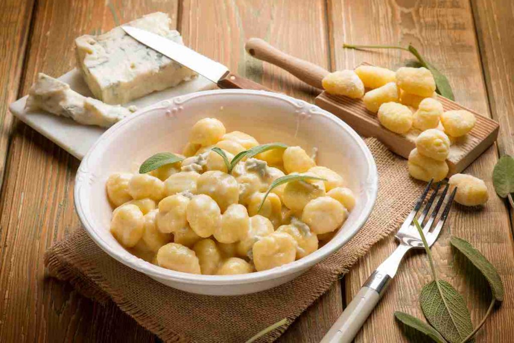piatto di gnocchi al gorgonzola su un tavolo su cui ci sono gnocchi di patate e un pezzo di gorgonzola fresco