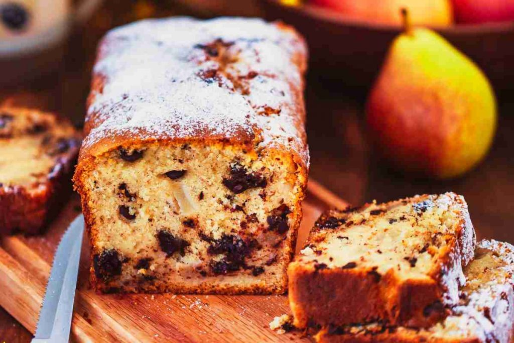 Plumcake con pere e cioccolato su un tagliere con dietro un cesto pieno di pere