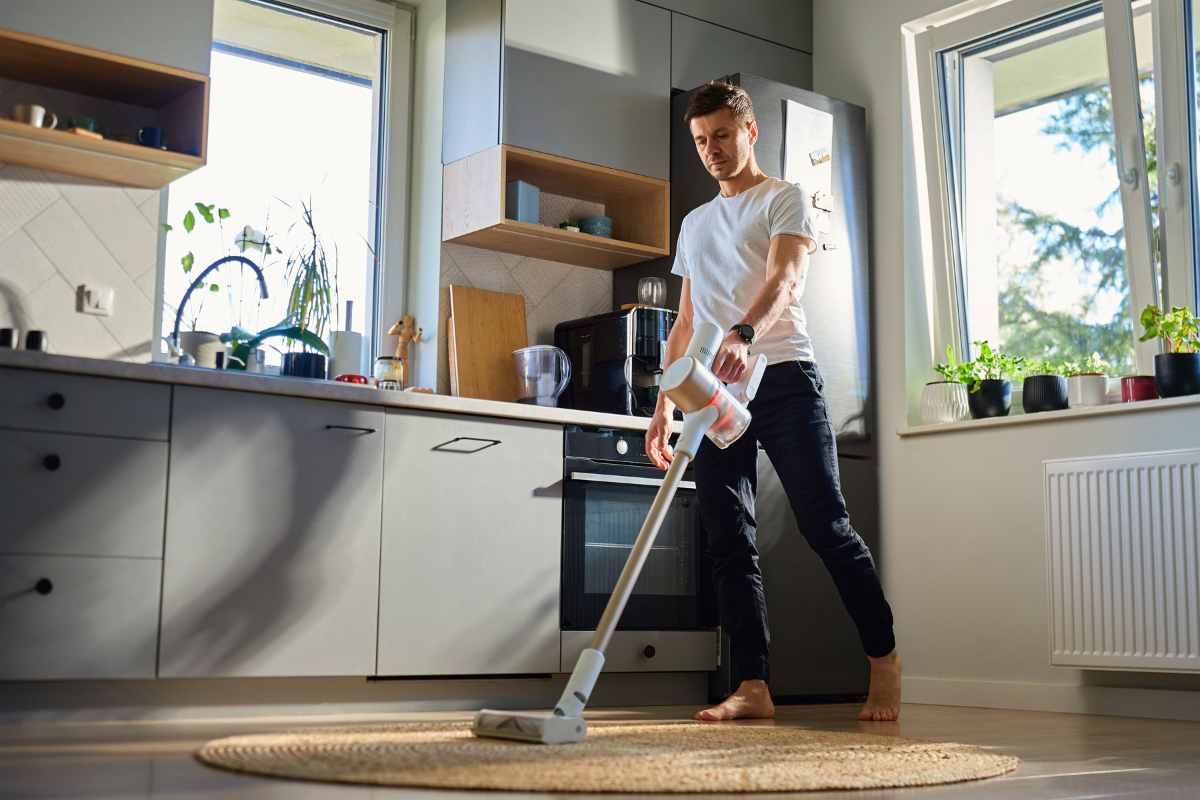 uomo che usa aspirapolvere in cucina