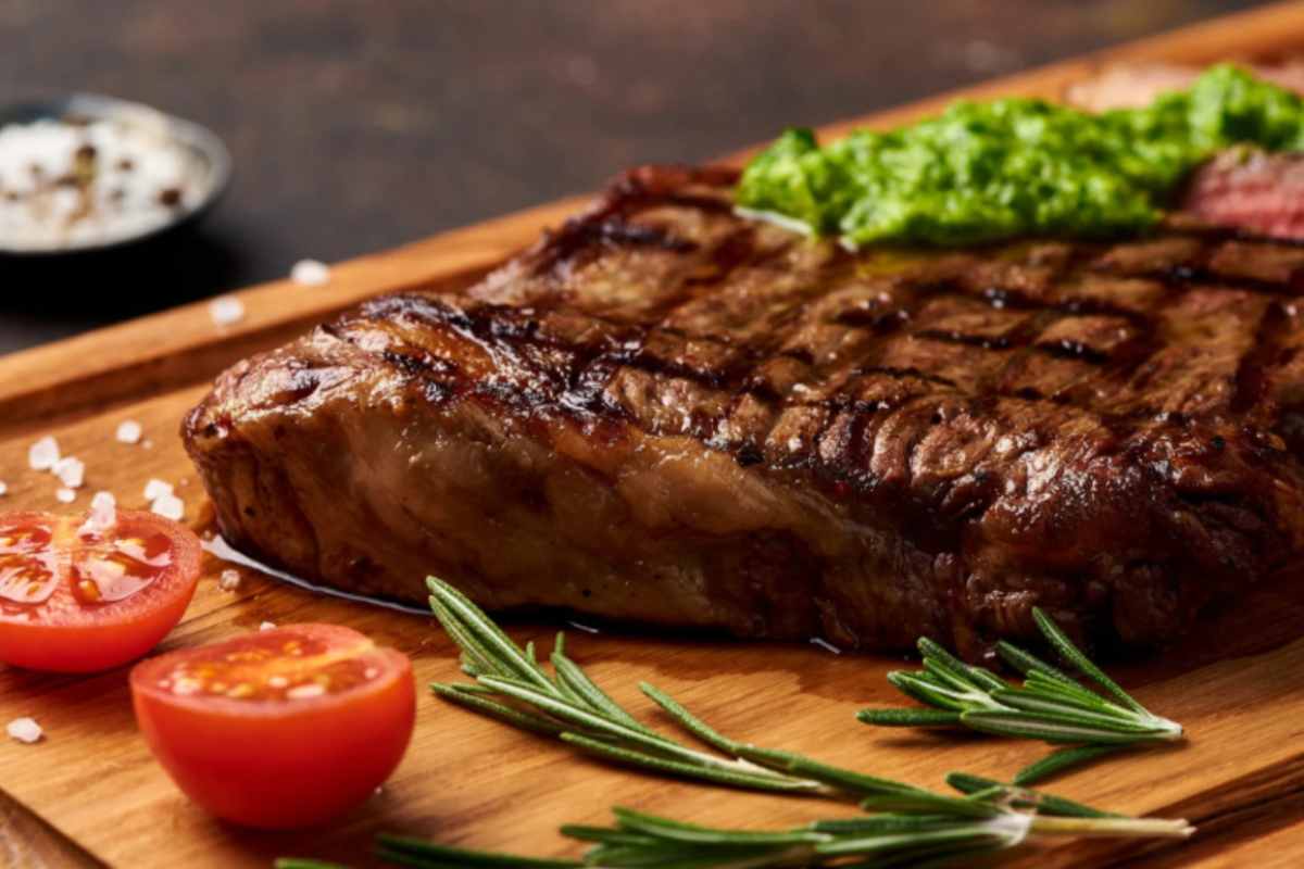 bistecca sopra un tagliere di legno con accanto insalata e pomodorini