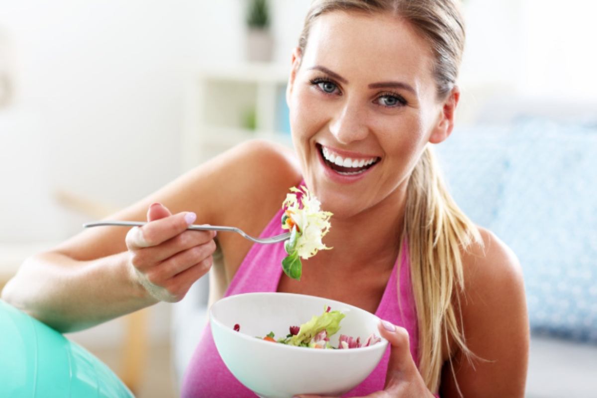 donna che sorride mentre mangia un'insalata