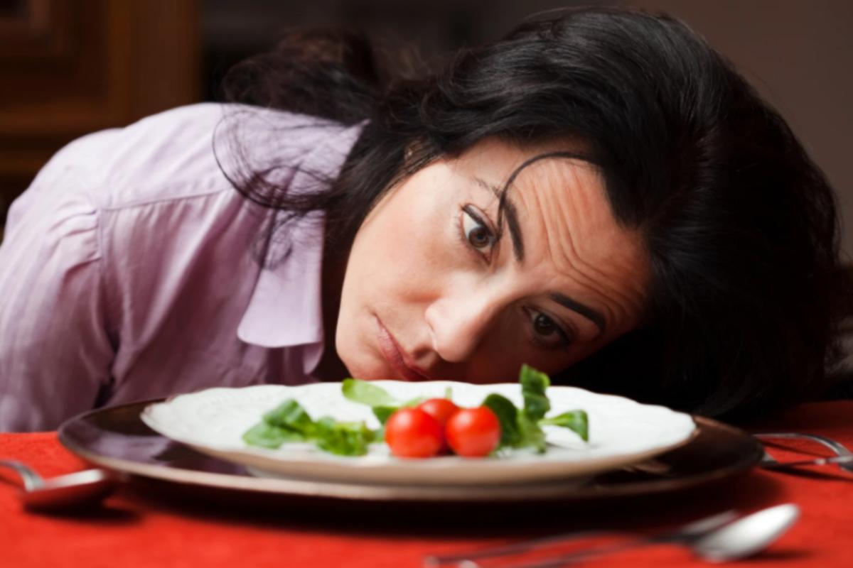 donna che guarda triste un piatto con dentro insalata e pomodori