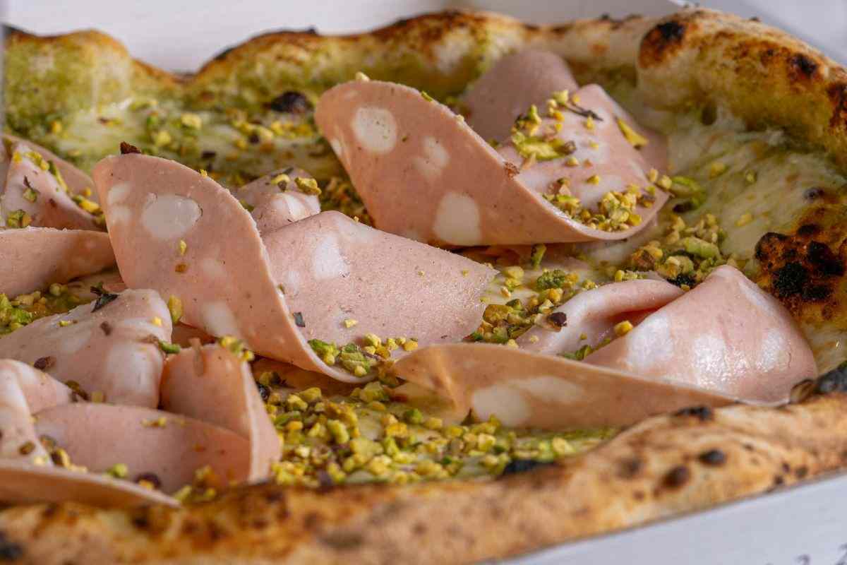 una pizza con pesto di pistacchio e mortadella a fette
