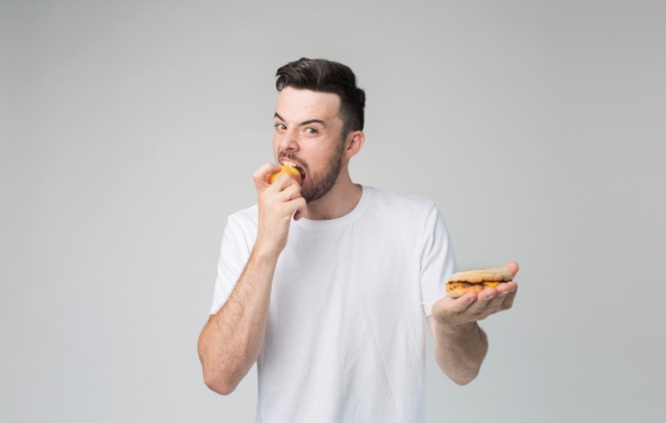 uomo che mangia una mela e nell'altra mano tiene un hamburger