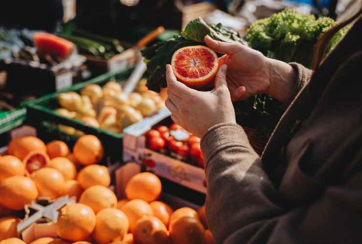 persona con mezzo arancio in mano al supermercato