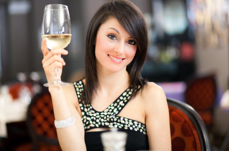 donna sorridente al ristorante che tiene in mano un calice di vino bianco