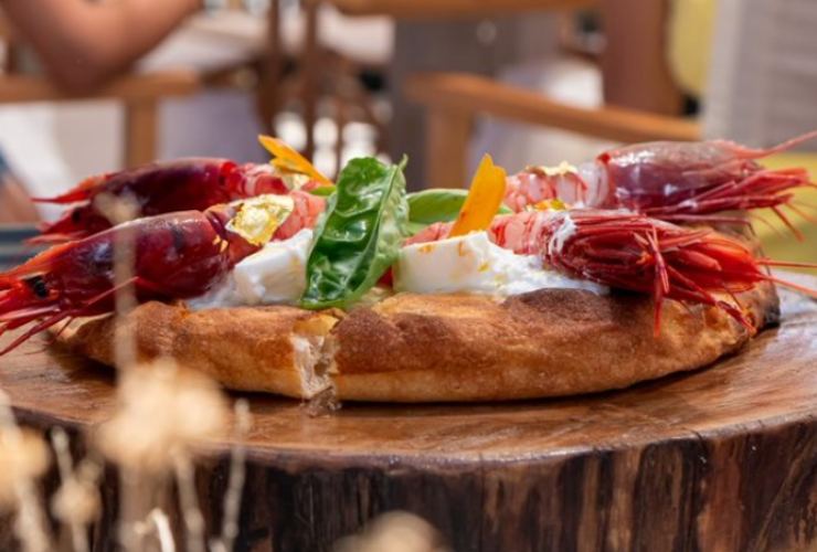 pizza con sopra dei gamberi viola su un tagliere di legno 