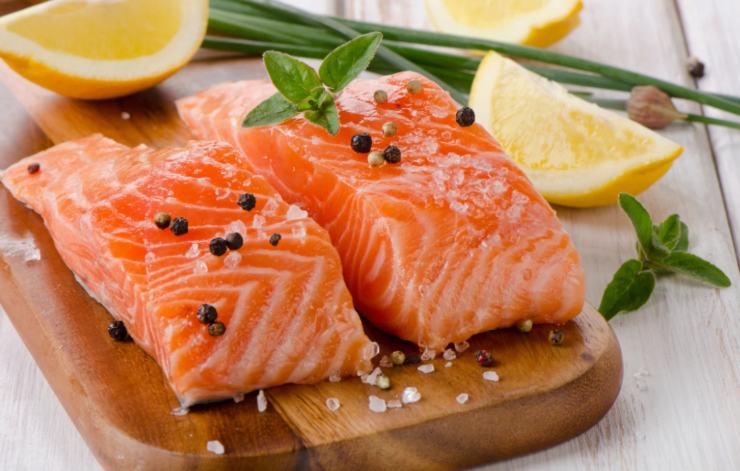 due filetti di salmone crudo sopra ad un tagliere con sopra dei granelli di pepe