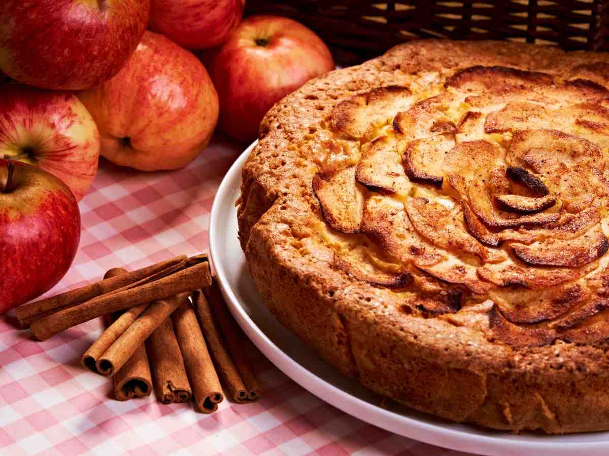 una torta di mele in un piatto con frutta e cannella accanto
