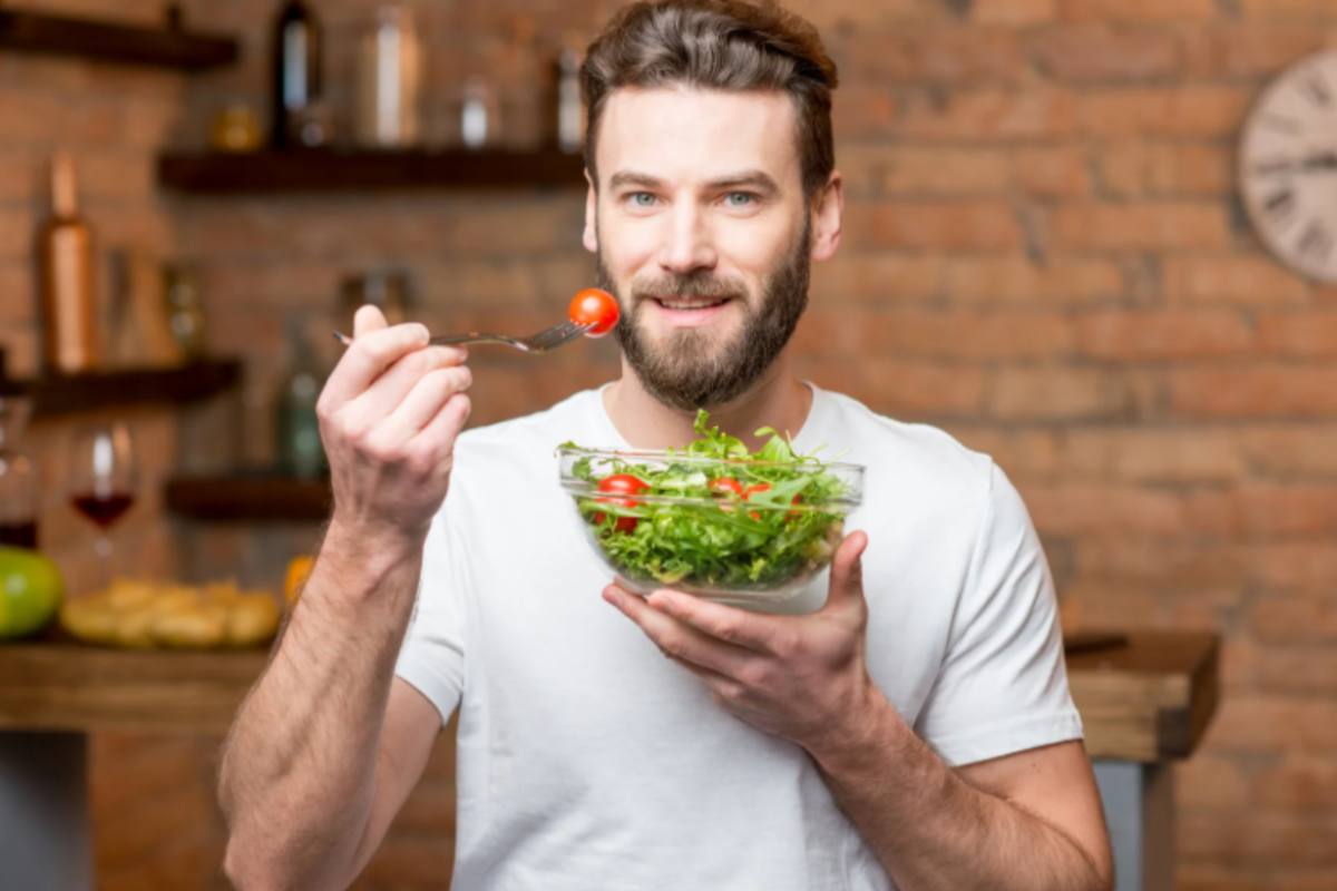 uomo che mangia un'insalata con pomodori