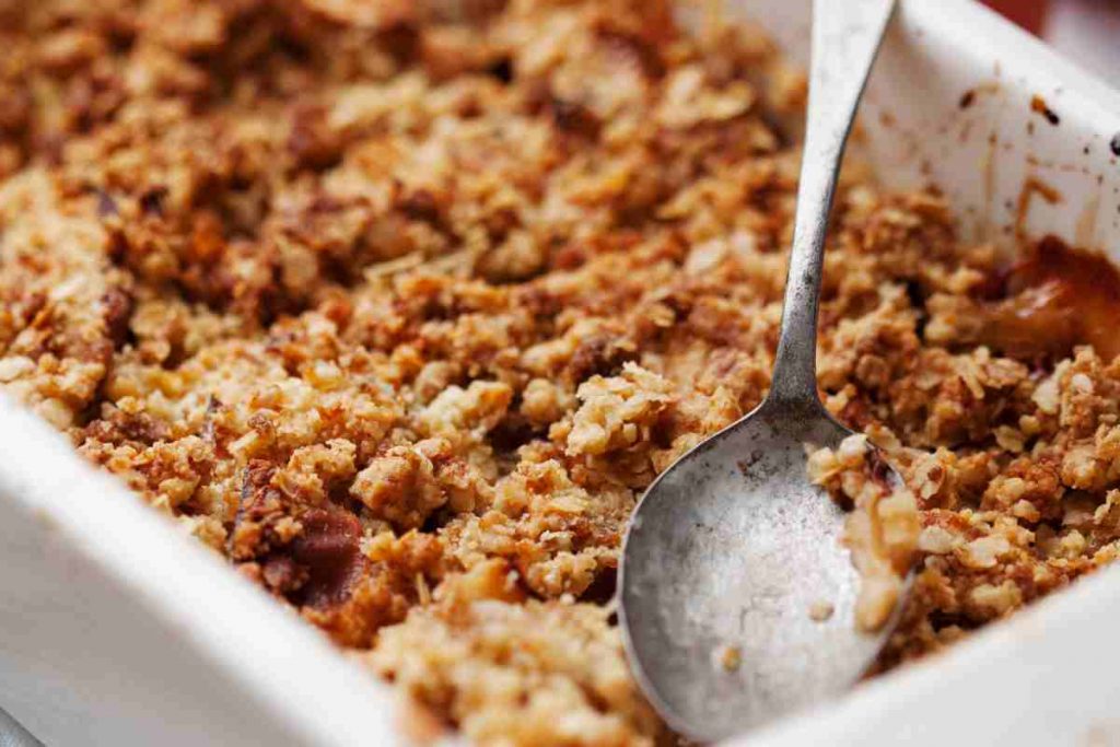 Crumble alle mele con cioccolato in una pirofila con dentro un cucchiaino