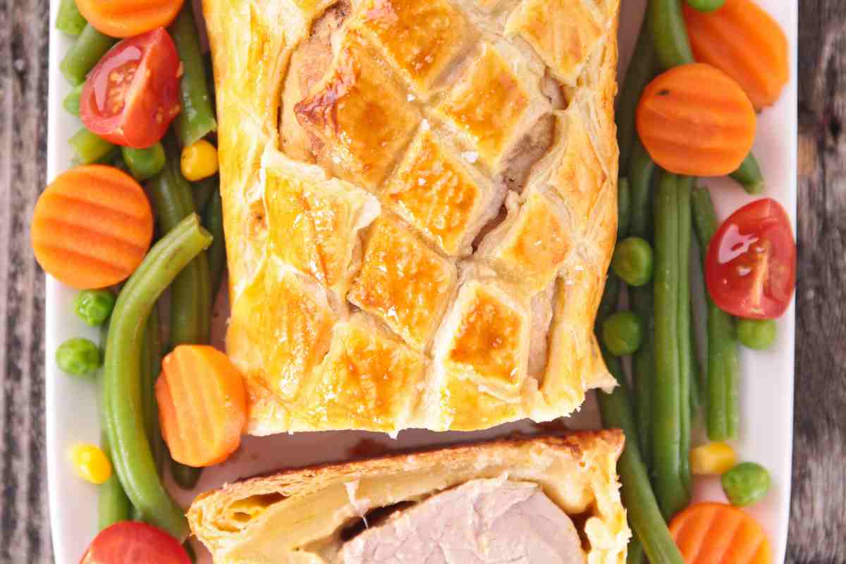 un vassoio con il filetto di maiale in crosta di pasta sfoglia contornato da carote e fagiolini