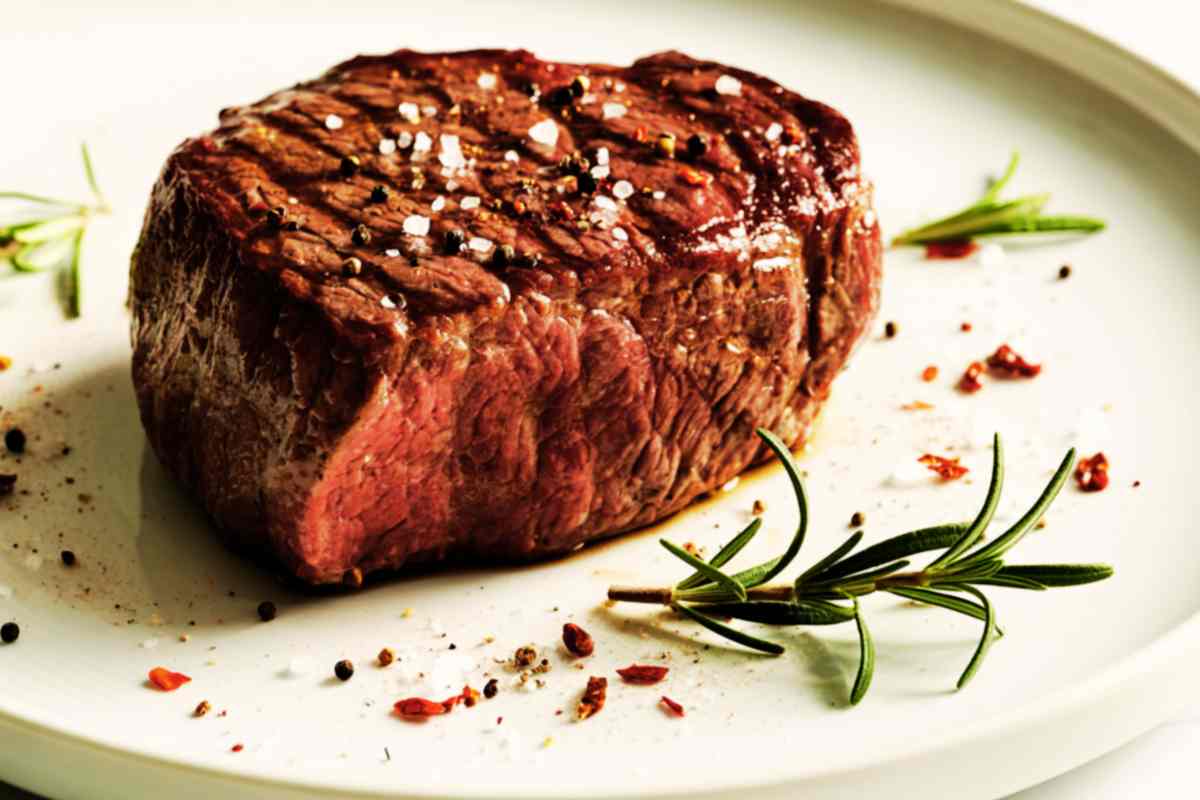 un pezzo di controfiletto di manzo al sangue in un piatto con grani di pepe e rosmarino