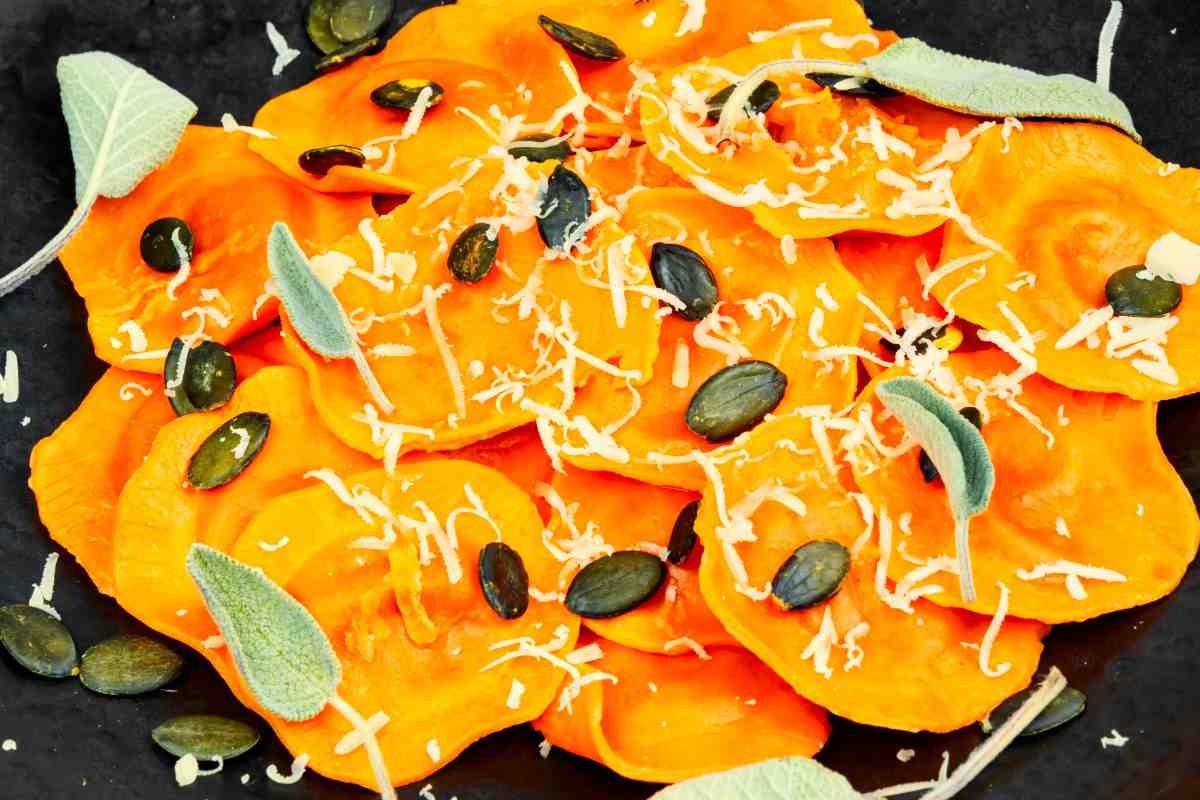 piatto nero con ravioli alla zucca arricchiti con semi e foglie di salvia fresca