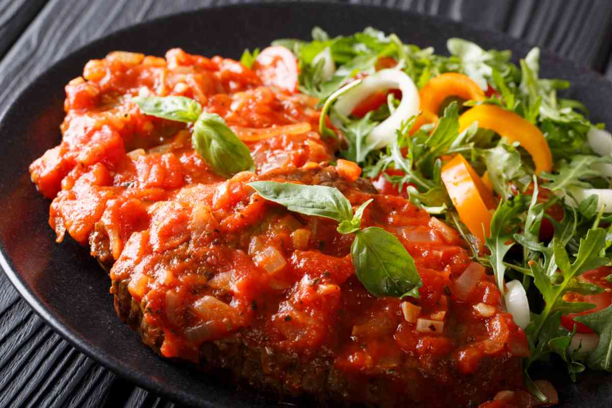 un piatto nero con una fetta di carne al sugo e contorno di verdure per il menu della settimana