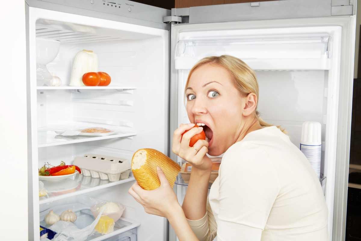 donna che mangia con il frigo aperto