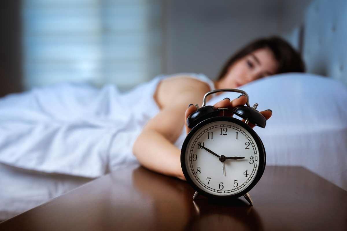 donna al letto con sveglia sul comodino in primo piano