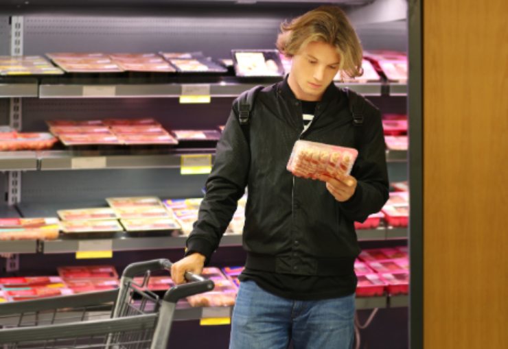 uomo al supermercato che legge l'etichetta di una confezione di carne