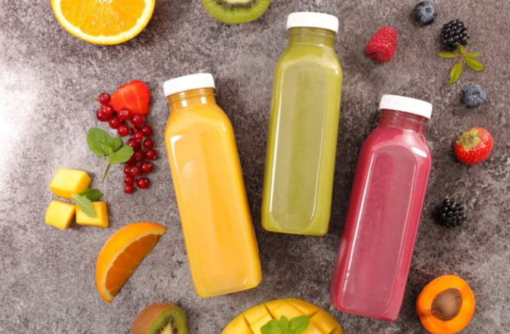 tre bottigliette di succhi di frutta circondati da pezzi di frutta