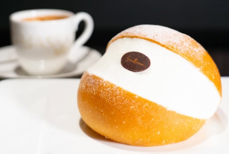 un maritozzo con la panna e dietro una tazzina di caffè