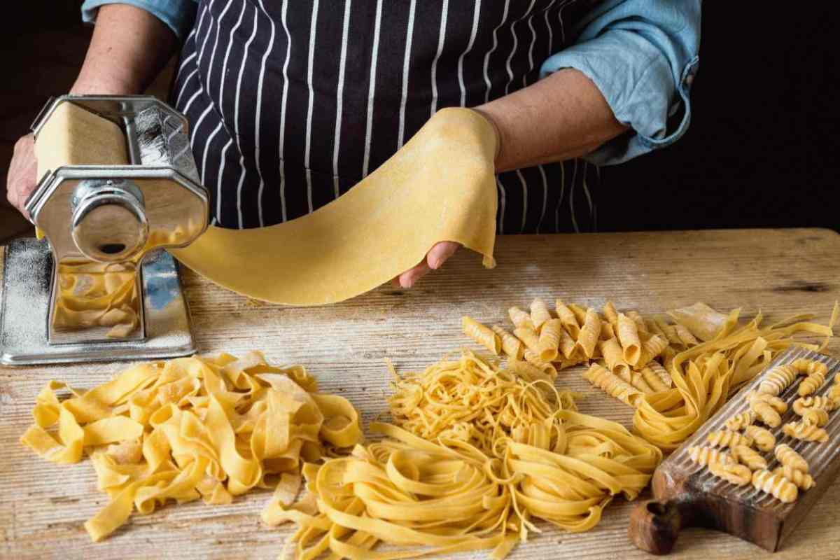 persona che fa la pasta fatta in casa e formati di pasta sul tagliere