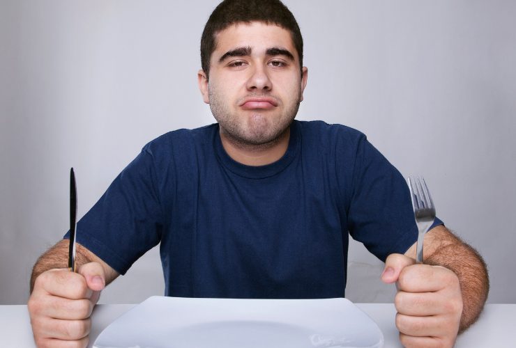 uomo con piatto davanti e posate in mano