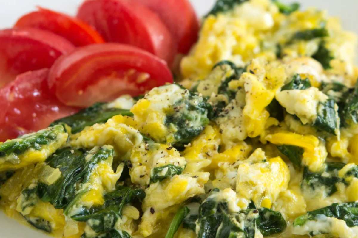 uova strapazzate con spinaci in un piatto con pomodori