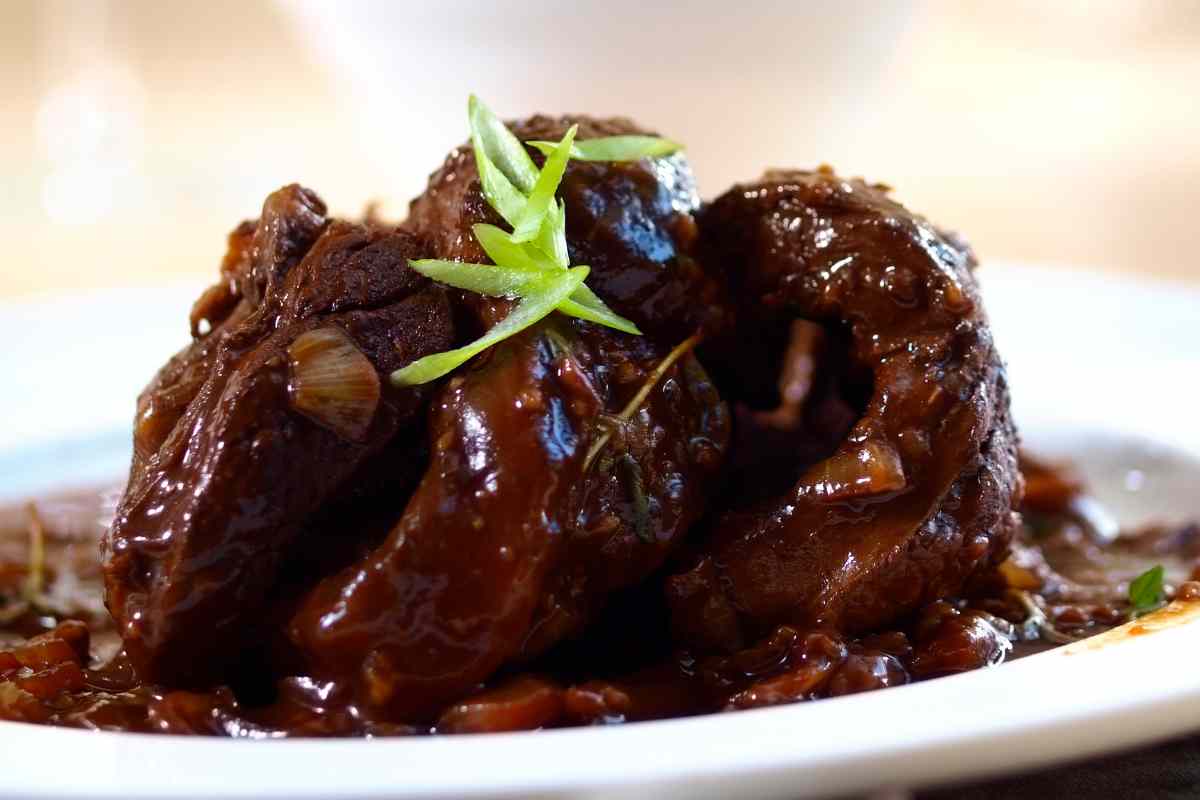 Un piatto con il brasato al vino guarnito con un rametto di rosmarino