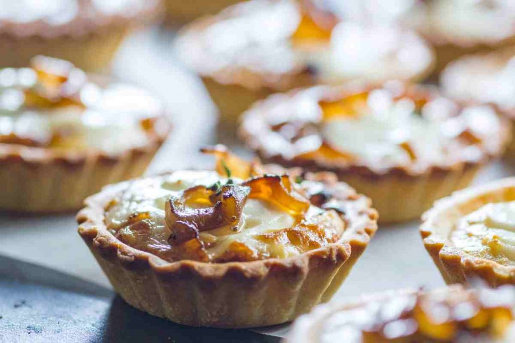 un vassoio con sopra tante crostatine salate farcite con cipolla e pancetta