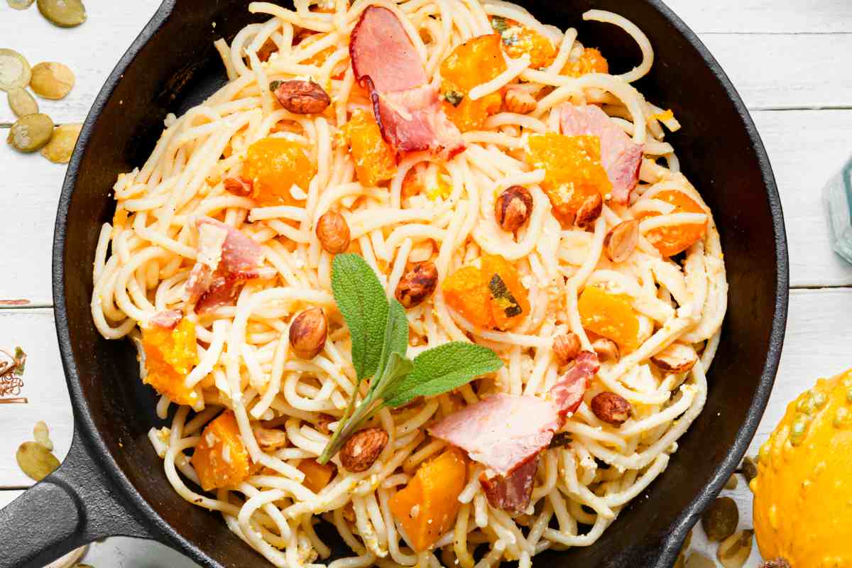 una padella con degli spaghetti alla zucca e bacon decorati con semi di zucca