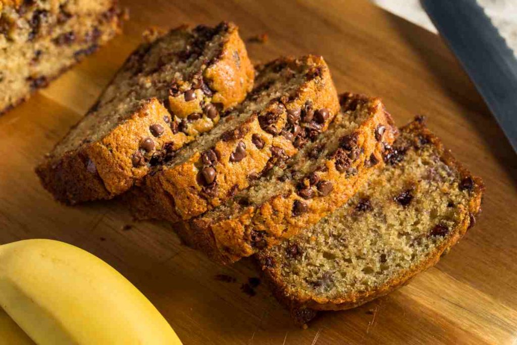 un plumcake alla banana con le gocce di cioccolato tagliate a fette su un tagliere di legno