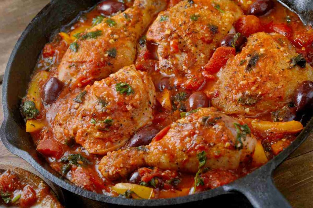 una padella di ferro con dentro pezzi di pollo alla cacciatora