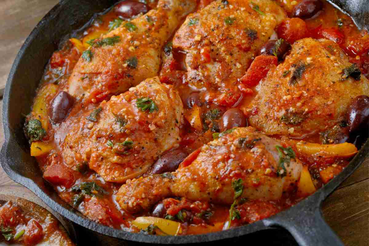 una padella di ferro con dentro pezzi di pollo alla cacciatora