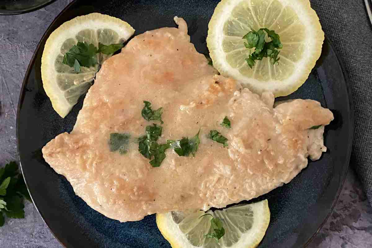 una scaloppina di vitello in un piatto nero decorata con fette di limone vista dall'alto