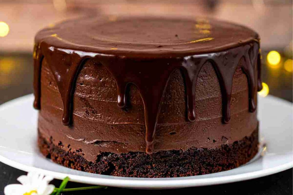 una torta trionfo al cioccolato con una colata di fondente sopra posta in un piatto bianco