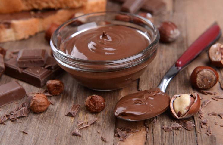 crema al cioccolato dentro ad una ciotolina di vetro e accanto un cucchiaio e delle nocciole