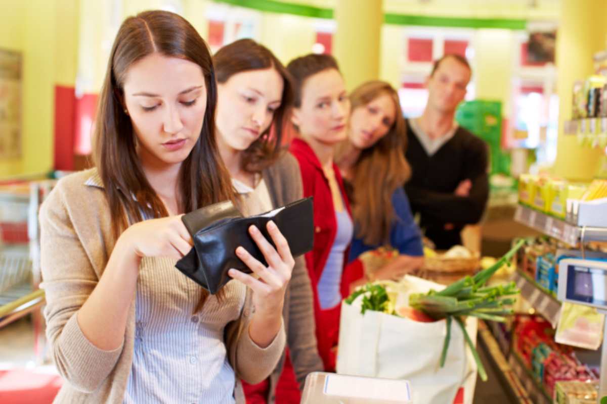 donna alla cassa del supermercato che cerca i soldi nel portafoglio