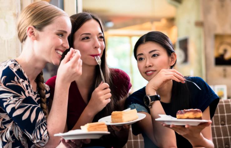 tre donne al ristorante che sorridono mentre mangiano tre fette di torta