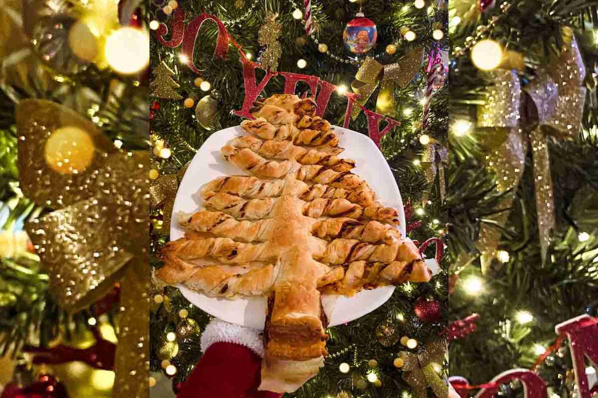 una mano regge un albero di pasta sfoglia in un piatto davanti all'abete illuminato