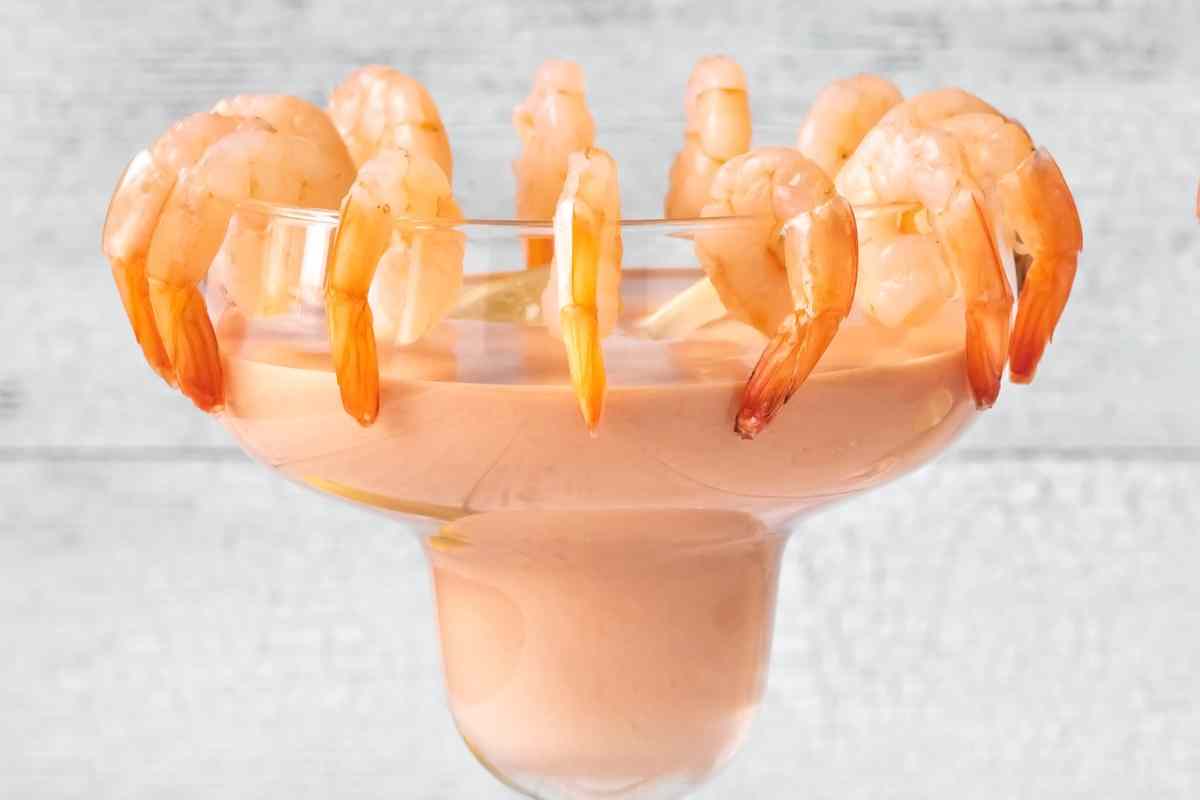 una coppa con dentro la salsa cocktail e i gamberetti sul borso